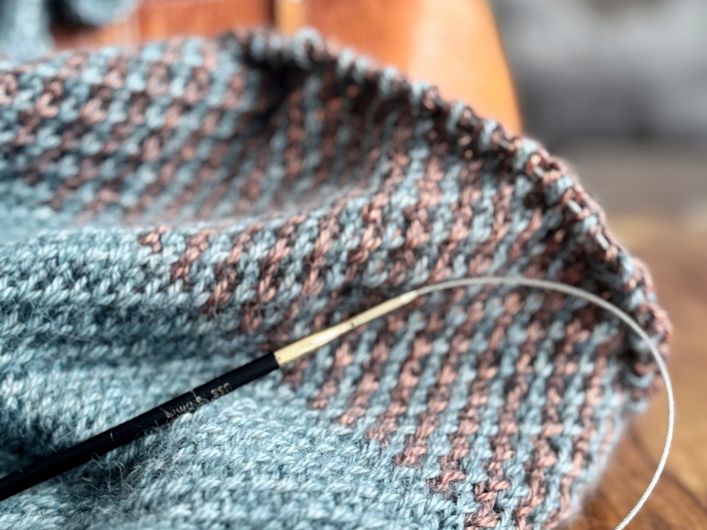 Lyn Balance – zweifarbiges Strickstück mit Hebemaschenmuster, Stricknadeln im Einsatz.