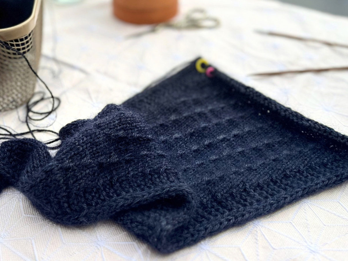 Blaues angestricktes Dreieckstuch auf einem Tisch mit Strickutensilien.
