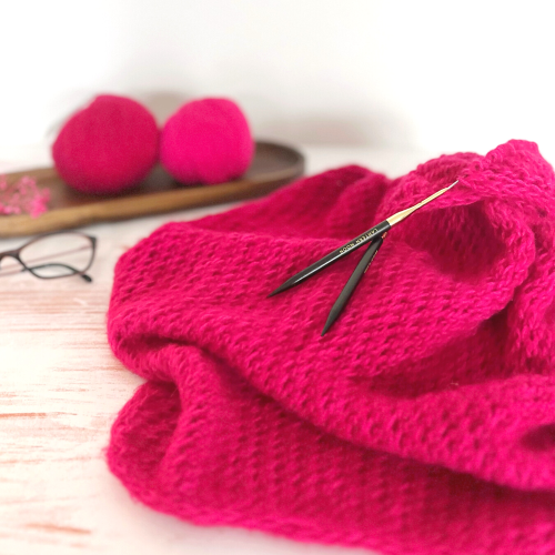 Dreieckstuch Levita Tuch stricken. Ein Magentafarbenes Tuch liegt angestrickt auf einem Tisch.